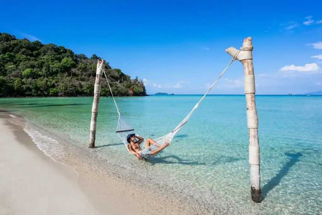 شخص يسترخي على أرجوحة شبكية على شاطئ استوائي