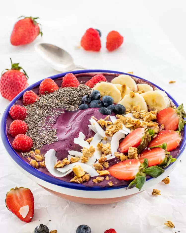 Healthy smoothie bowl topped with frozen strawberries, banana slices, and blueberries