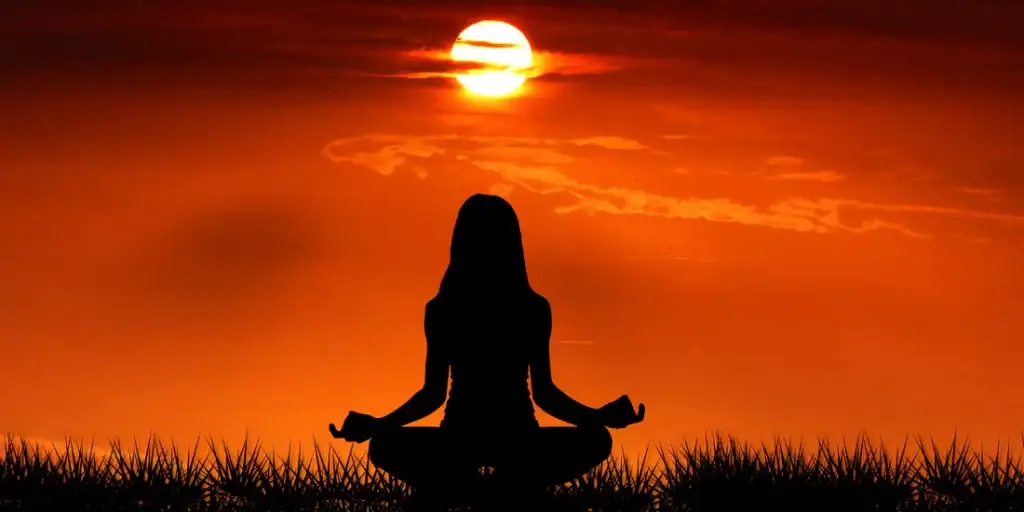 شخص يمارس التأمل لتعزيز الصحة النفسية عند شروق الشمس